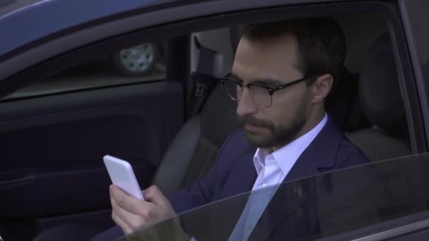 Smiling businessman in eyeglasses using smartphone in car  - Video