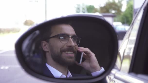 İş adamı arabanın kanat aynasından yansıtırken akıllı telefondan konuşuyor.  - Video, Çekim
