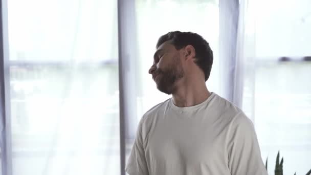Γενειοφόρος και χαμογελαστός άνδρας σε λευκό t-shirt άσκηση στο σπίτι  - Πλάνα, βίντεο