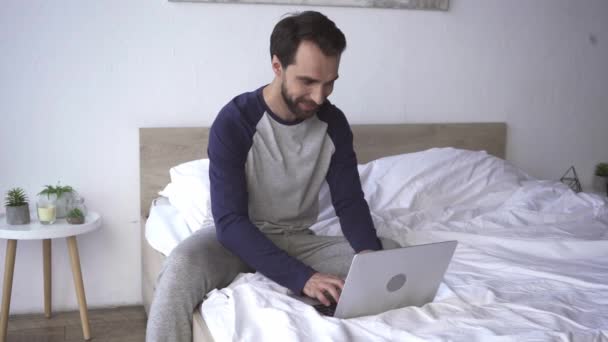 Smiling freelancer using laptop on bed at home  - Footage, Video