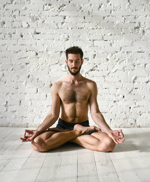 Een jongeman doet yoga. Yoga coach op een lichte achtergrond. - Foto, afbeelding