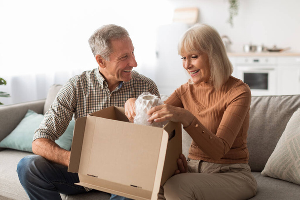 Ευτυχισμένο ώριμο ζευγάρι ξεπακετάρισμα κουτί μετά την επιτυχή ψώνια στο σπίτι - Φωτογραφία, εικόνα
