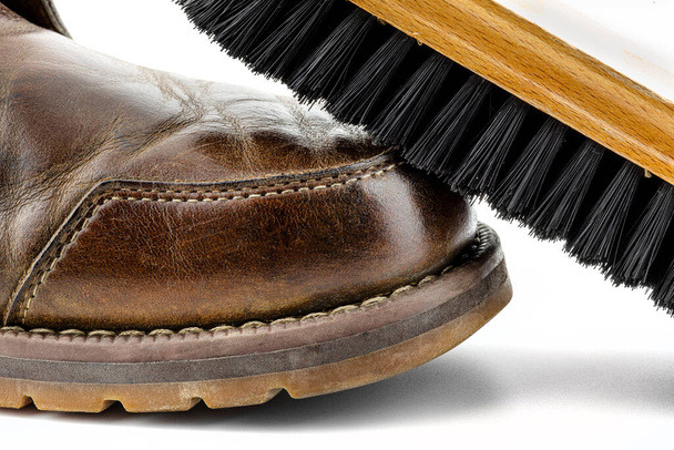 Macro photo d'un vieux bottines en cuir marron poli avec de la pâte, brosse à chaussures repose sur la chaussure, isolé sur un fond blanc. - Photo, image
