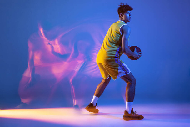 Full-length portrait of professional basketball player training with ball isolated on blue studio background in mixed neon light. - Foto, Imagem