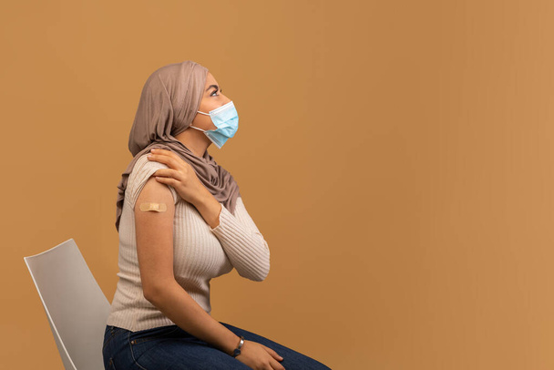 Banner de vacunación contra el Coronavirus. Mujer árabe con máscara facial con vendaje adhesivo en el hombro después de la vacuna covid - Foto, Imagen