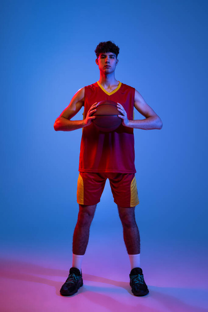 Portrait of professional basketball player posing with ball isolated on blue studio background in neon light. - Fotografie, Obrázek