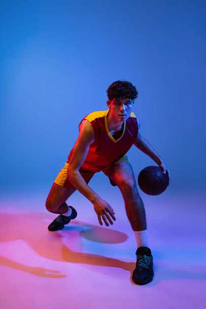 Studio shot of young man, professional basketball player playing basketball isolated on blue background in neon light. - Foto, Bild