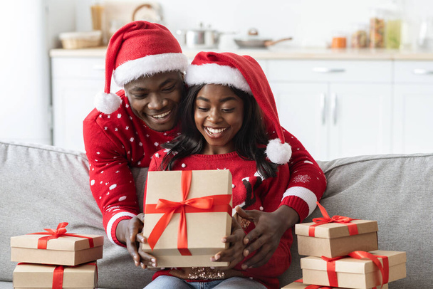 Lächelndes afrikanisch-amerikanisches Paar öffnet Weihnachtsgeschenke von Verwandten - Foto, Bild