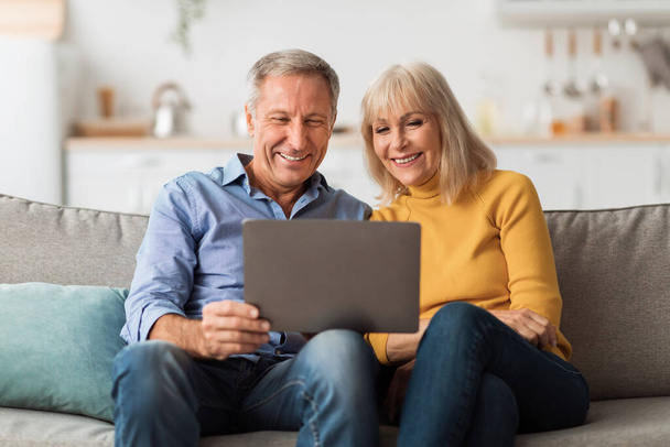 Ευτυχισμένο ώριμο ζευγάρι χρησιμοποιώντας το φορητό υπολογιστή περιήγηση στο Διαδίκτυο μαζί στο σπίτι - Φωτογραφία, εικόνα