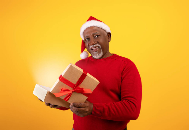 Boldog idősebb fekete férfi a Mikulás kalap megnyitása Xmas ajándék tündér fény, megkapja a kívánt ajándékot karácsonyra - Fotó, kép