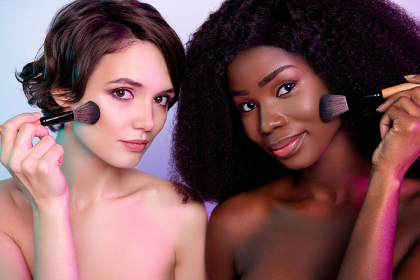 Photo rapprochée de deux jolies petites amies appliquant des cosmétiques de fond de teint pureté isolée sur fond coloré - Photo, image