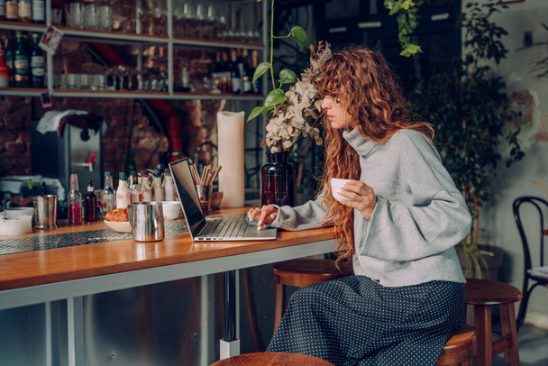 Επιχειρηματίας με σγουρά μαλλιά εργάζεται στο καφέ απομακρυσμένο γραφείο χρησιμοποιώντας φορητό υπολογιστή. Επιλεκτική εστίαση. - Φωτογραφία, εικόνα