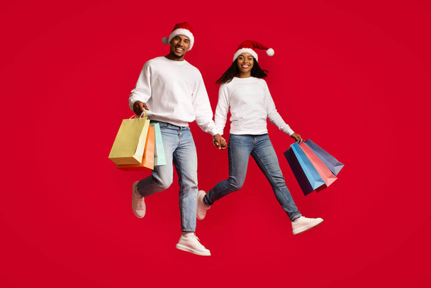 Feliz negro amantes en Santa sombreros disfrutando de compras juntos - Foto, imagen
