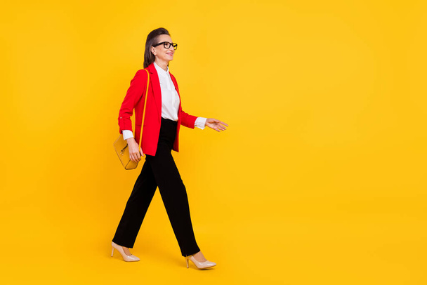 Full length profile photo of cool aged woman go wear cardigan pants stilettos isolated on yellow background - Fotografie, Obrázek