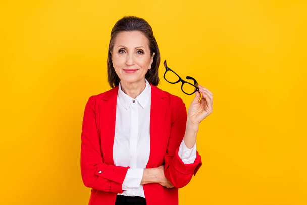 Photo of nice elder brunette lady try eyewear wear red jacket isolated on yellow color background - 写真・画像
