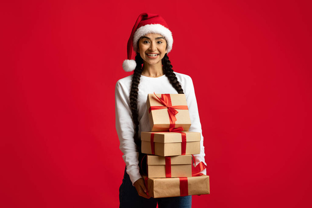 Cadeaux de Noël. Heureuse dame arabe dans Santa Hat tenant pile de cadeaux - Photo, image