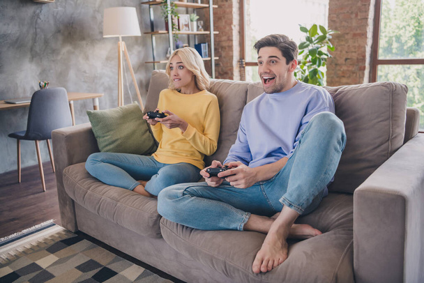 Photo of beautiful excited young lovers dressed casual clothes sitting sofa holding playstation smiling indoors apartment - Valokuva, kuva