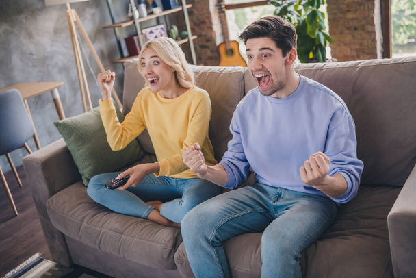 Photo of attractive beautiful young lovers dressed casual clothes sitting sofa watching football match smiling indoors apartment - Фото, изображение
