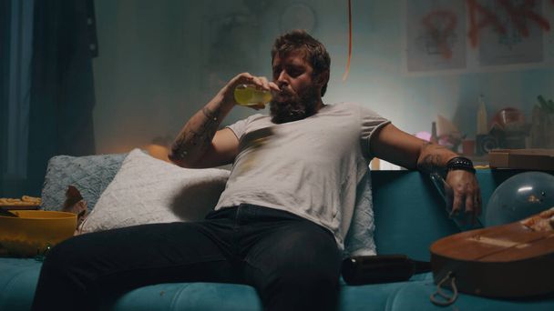 Мужчина пьет алкоголь на диване в курильной комнате - Фото, изображение