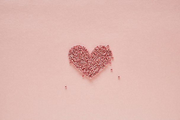 Heart symbol made of beads on pale pink background. Minimal concept for Valentines Day. Flat lay, top view, copy space. - Φωτογραφία, εικόνα