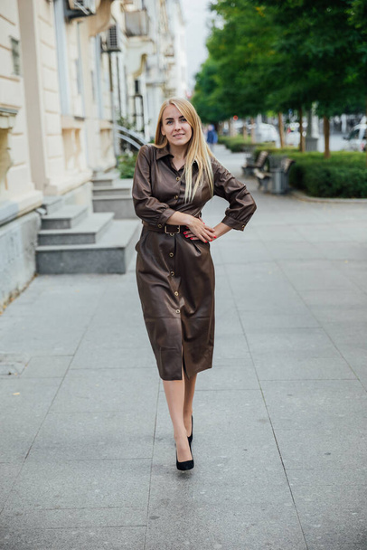 beautiful blonde woman in a leather dress walking on the street - Foto, Imagen