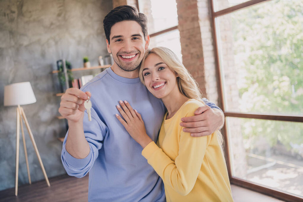 Photo of beautiful shiny young lovers dressed casual clothes hugging buying new apartment smiling indoors apartment - 写真・画像