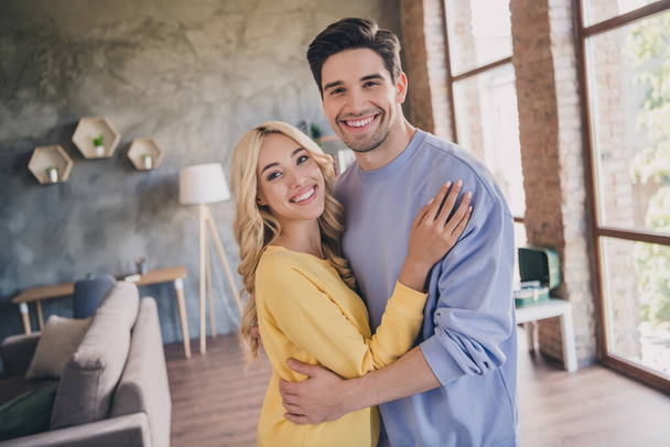 Photo of beautiful shiny young lovers dressed casual clothes hugging smiling indoors apartment - Foto, imagen