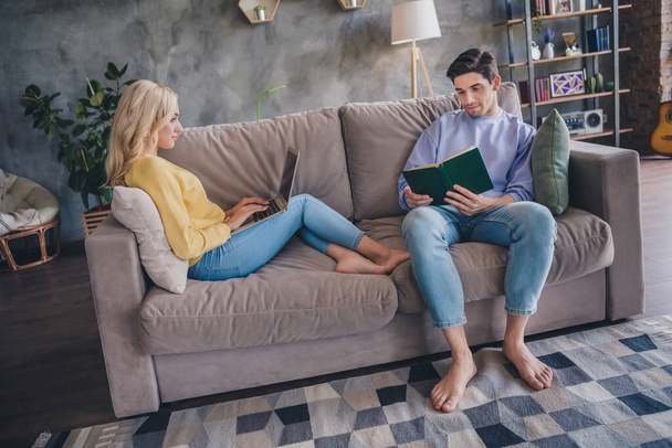 Photo of beautiful attractive young couple wear casual outfits smiling sitting couch looking modern device reading story indoors house room - Фото, зображення
