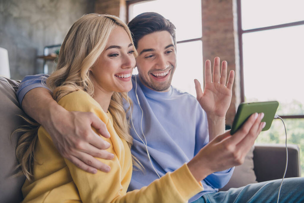Portrait of attractive cheerful couple using gadget calling video listen waving hello contact at home loft industrial interior indoors - Photo, image