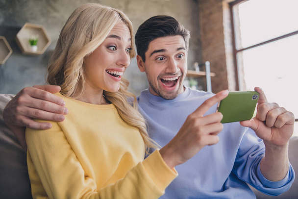 Portrait of attractive amazed cheerful couple using gadget watching funny post media video at home loft industrial interior indoors - Foto, Imagem