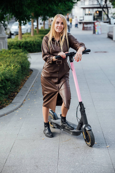 beautiful blonde woman in a cloak on an scooter - Photo, image