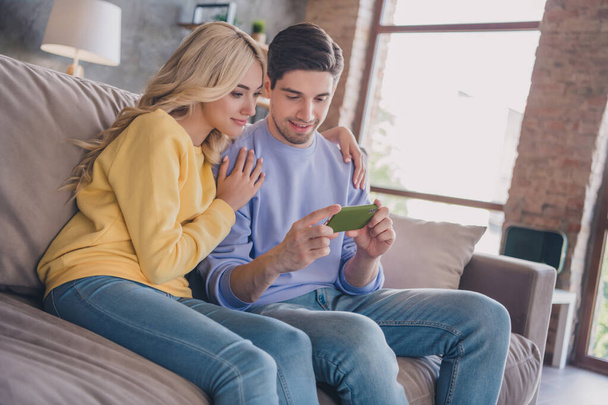Photo of attractive sweet young couple wear casual outfits smiling sitting couch looking modern devices indoors house room - Foto, Bild
