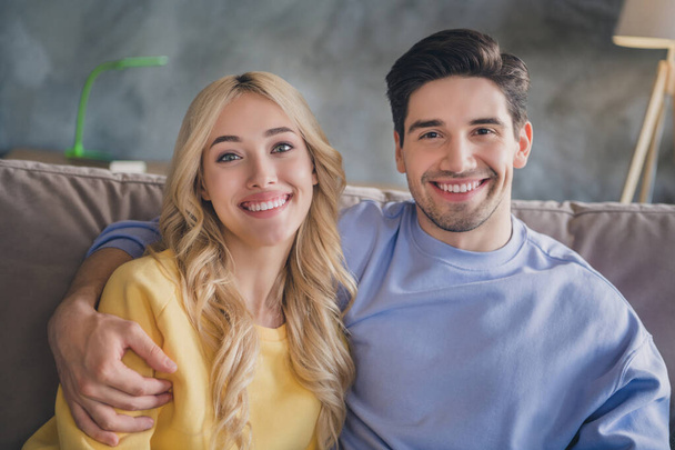 Photo of charming beautiful young lovers dressed casual clothes sitting sofa hugging smiling indoors apartment - Φωτογραφία, εικόνα