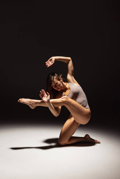 Dynamic portrait of young flexible contemp dancer dancing isolated on dark studio background in spotlight. Art, beauty, inspiration concept. - Foto, Imagen