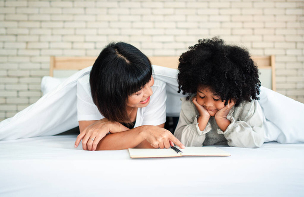 Gelukkige schattige kleine kleuter kind dochter lezen boek leren onderwijs whit mam. Concept van gelukkig gezin en focus op kinderen - Foto, afbeelding