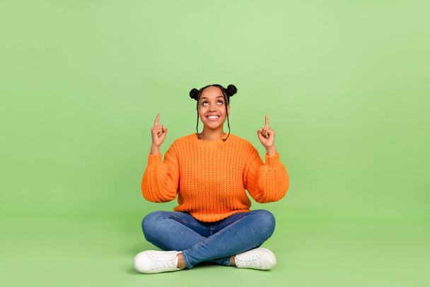 Full length photo of hipster young brunette lady sit indicate look empty space wear sweater jeans footwear isolated on green background - Φωτογραφία, εικόνα