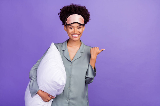 Photo of sweet beautiful student grey sleepwear smiling holding pillow pointing empty space isolated violet color background. - Foto, Imagen