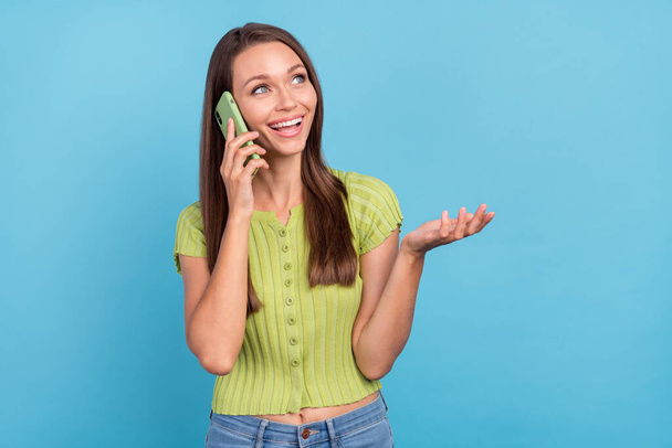 Photo of positive pretty nice young woman look empty space talk phone enjoy isolated on blue color background. - Foto, Imagem