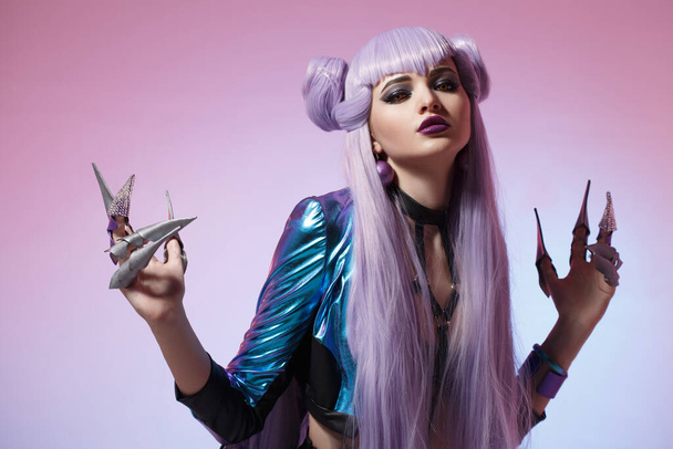 A cute girl witch with long purple hair with knife-claws on a bright blue and lilac background. - Foto, Imagen