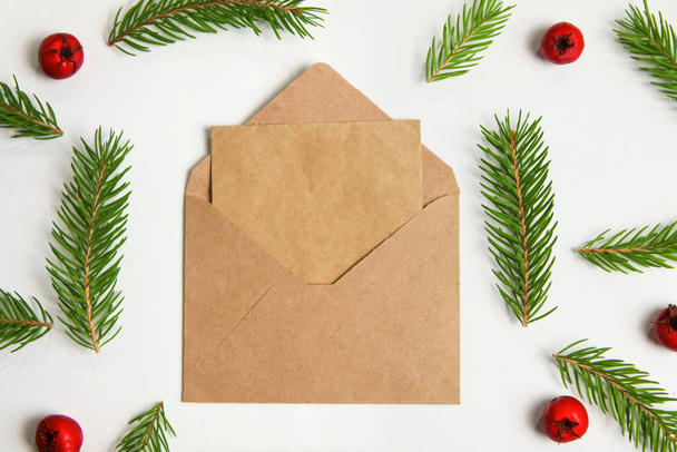 クローズアップベージュクラフトエンベロープ、サンタへの手紙。モミの枝やトウヒの枝のフレームと白い背景に隔離された赤い果実。木の枝が太い。クリスマスのグリーティングカード。デザインのテンプレート. - 写真・画像