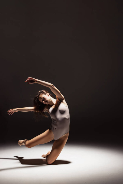 Dynamic portrait of young flexible contemp dancer dancing isolated on dark studio background in spotlight. Art, beauty, inspiration concept. - Foto, Imagem