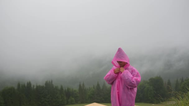 Attrayant randonneur fille dans un imperméable rose se dresse sur une montagne - Séquence, vidéo