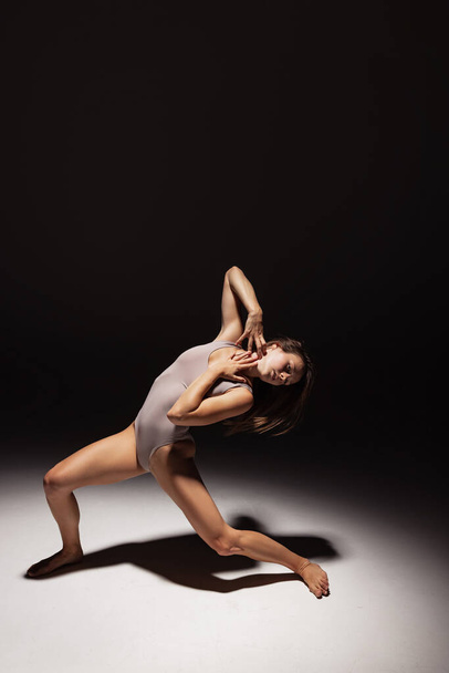 Dynamic portrait of young flexible contemp dancer dancing isolated on dark studio background in spotlight. Art, beauty, inspiration concept. - Foto, Imagem