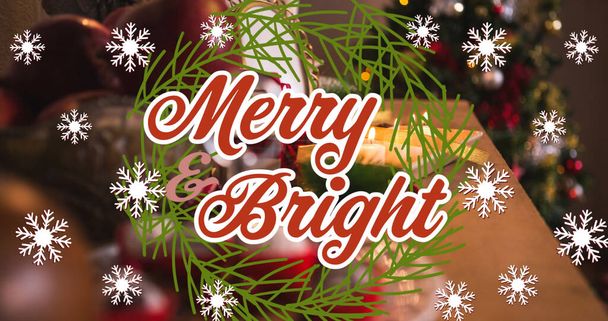 Image of merry and bright text over snowflakes and christmas decoration on table. christmas, winter, tradition and celebration concept digitally generated image. - Foto, imagen