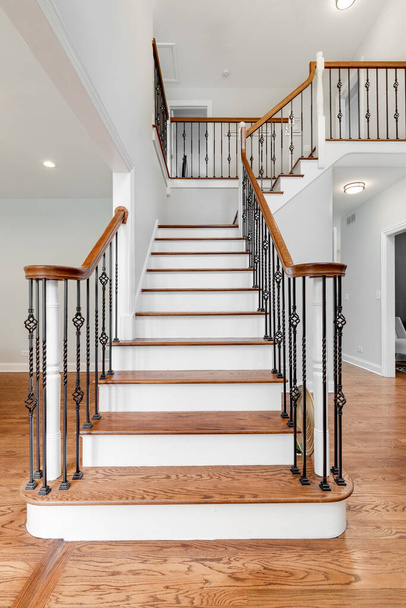 Mirando una escalera doméstica con barandillas de hierro forjado, barandillas de madera y pisos de madera en toda la casa. - Foto, imagen