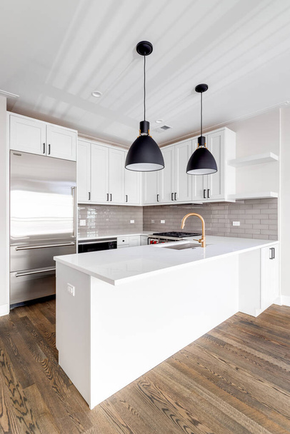 CHICAGO, IL, USA - JANUARI 6, 2020: Een moderne, geheel witte keuken in een condominium in de binnenstad met roestvrijstalen Wolf-apparaten en grote zwarte lichten boven het granieten aanrecht. - Foto, afbeelding