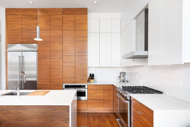 CHICAGO, IL, EE.UU. - 1 DE NOVIEMBRE DE 2020: Una cocina moderna y remodelada con armarios de madera y blancos, una isla de granito con cascada blanca, electrodomésticos KitchenAid y baldosas de pentágono blanco. - Foto, imagen