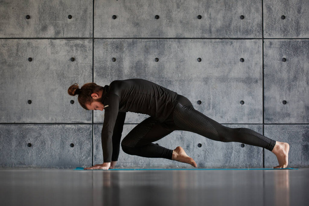 A young bearded man in black sportswear is practicing yoga against a gray wall. - Foto, Imagem