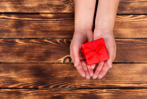 Woman's hand holding red gift box with red ribbon on the old wooden background Concept Of Valentine's Day. - Фото, зображення