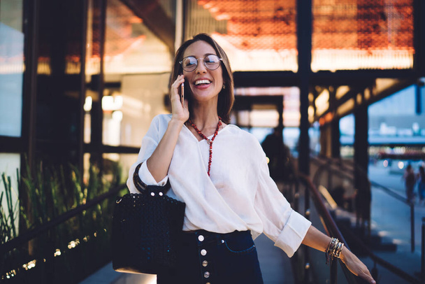 Vidám kaukázusi nő optikai szemüvegben nevet, miközben megkapja a nemzetközi hívás beszélgetés a modern mobiltelefon, boldog női felhasználó élvezi roaming internet kapcsolat kommunikáció - Fotó, kép